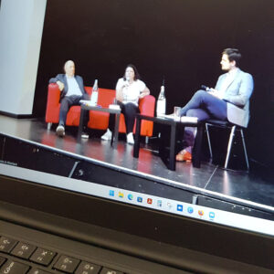 Blick auf den Livestream auf einem Laptopbildschirm. Zu sehen sind Nikolaus Schneider, Julia Friedrichs und Till Kiehne. 